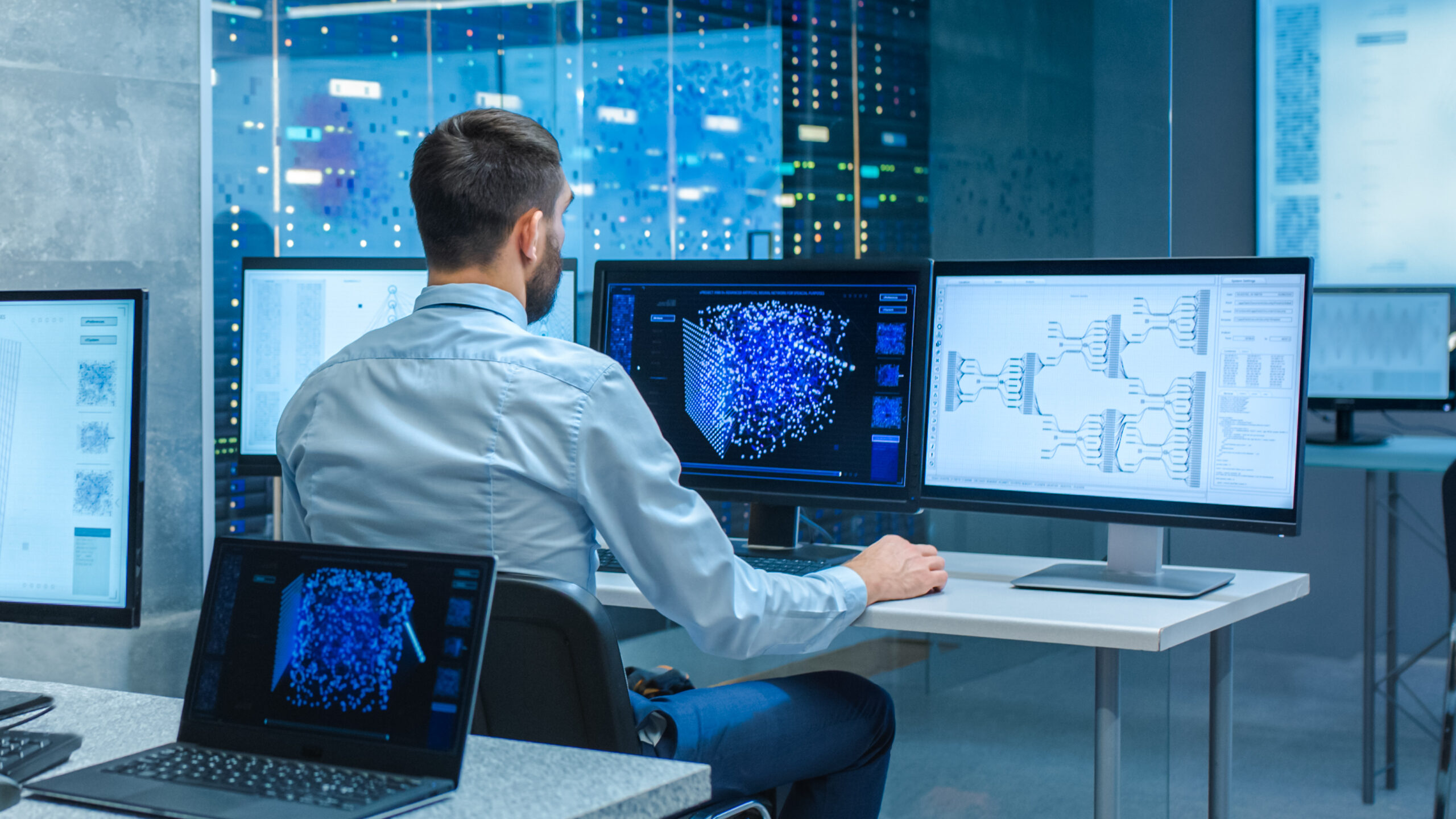 Male Computer Engineer and Scientists Create Neural Network at His Workstation. Office is Full of Displays Showing 3D Representations of Neural Networks.