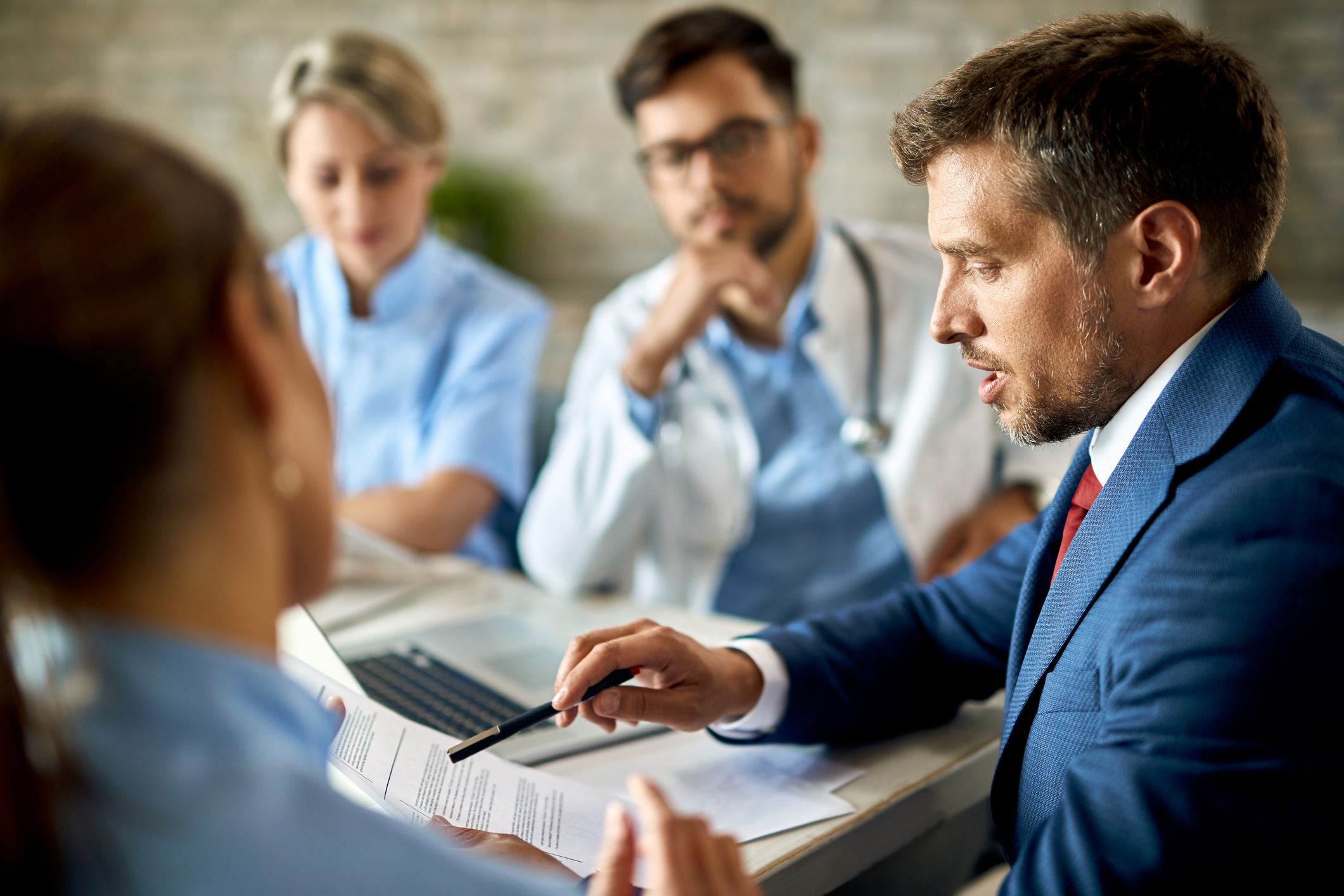 Businessman Cooperating With Doctors While Going Through Reports On A Meeting. Mid adult businessman and healthcare workers analyzing documents during a meeting in the office.
