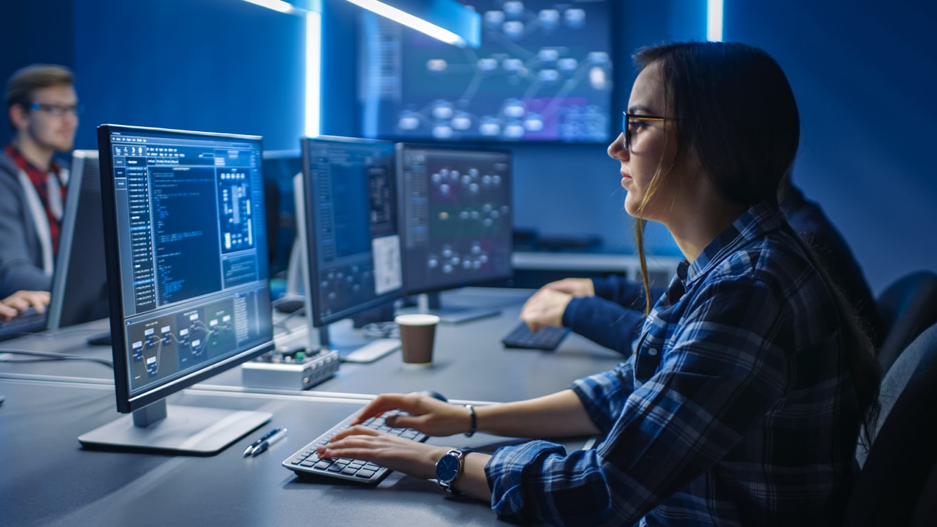 Smart Young Female IT Programer Working On Desktop Green Mock Up Screen Computer In Data Center System Control Room. Team Of Young Professionals Programming Sophisticated Code