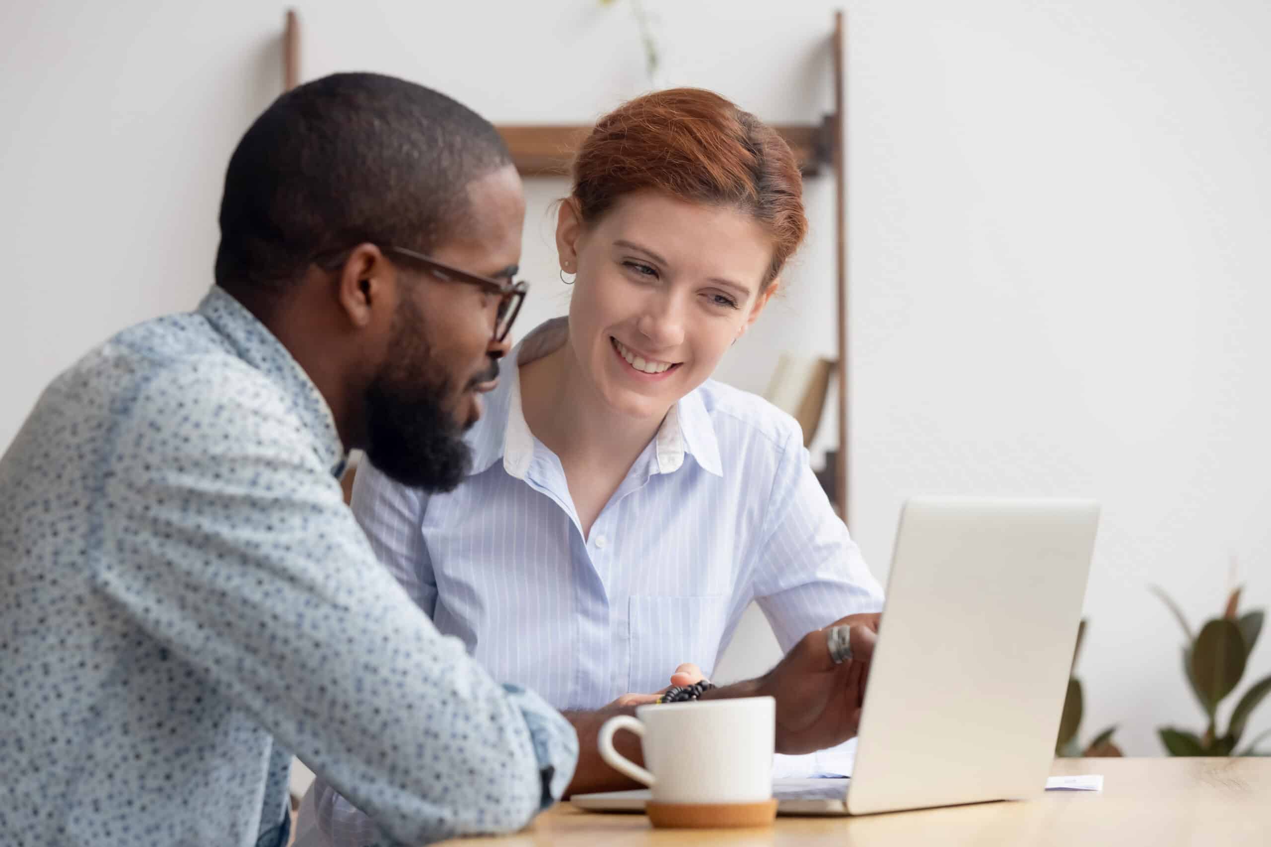 Two diverse smiling businesspeople discussing online project